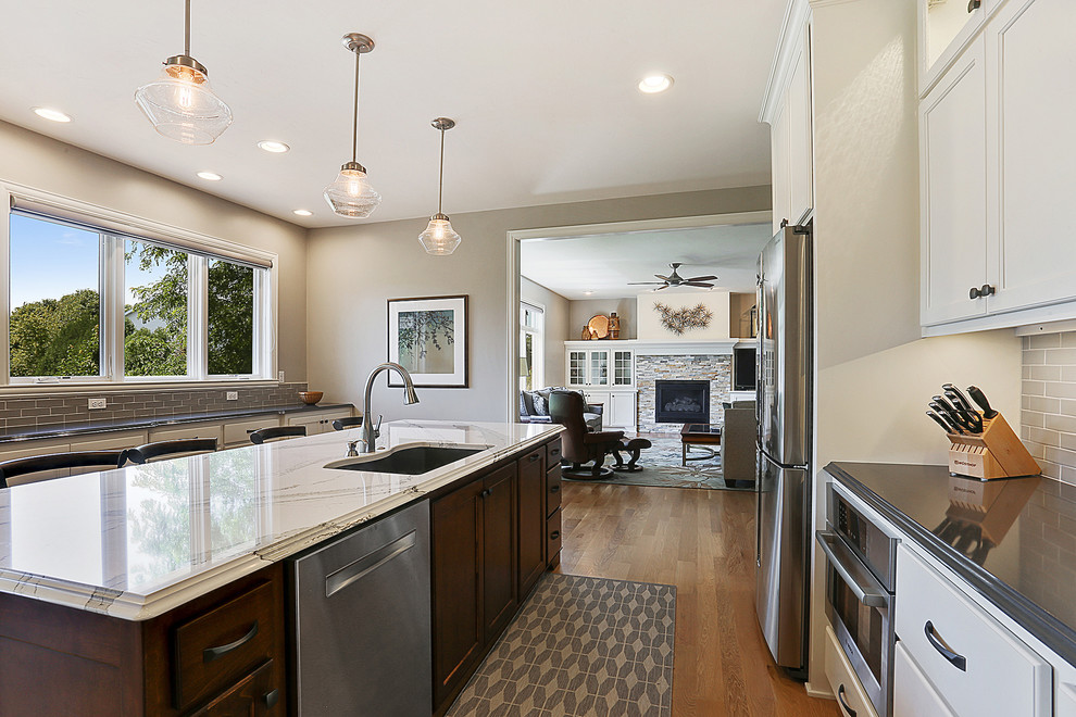Kitchen - galley medium tone wood floor and brown floor kitchen idea with white cabinets, stainless steel appliances, an island, gray backsplash and stone tile backsplash