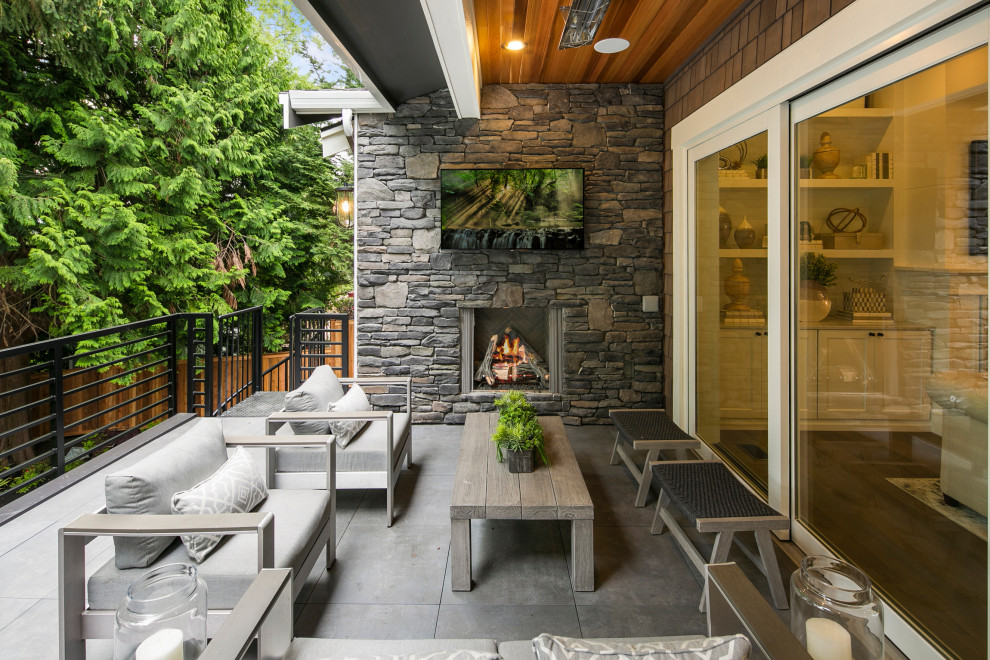 Large arts and crafts backyard deck in Seattle with with fireplace and a roof extension.
