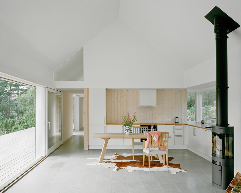 Photo of a large scandinavian l-shaped eat-in kitchen in Stockholm with flat-panel cabinets, white cabinets, panelled appliances, a drop-in sink, wood benchtops, ceramic floors and no island.