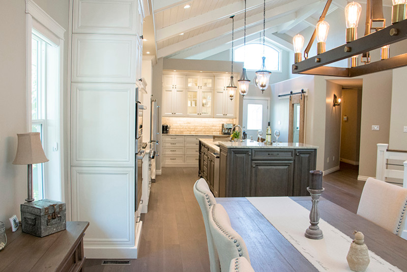 Large transitional l-shaped eat-in kitchen photo with a double-bowl sink, shaker cabinets, white cabinets, beige backsplash, stainless steel appliances and an island