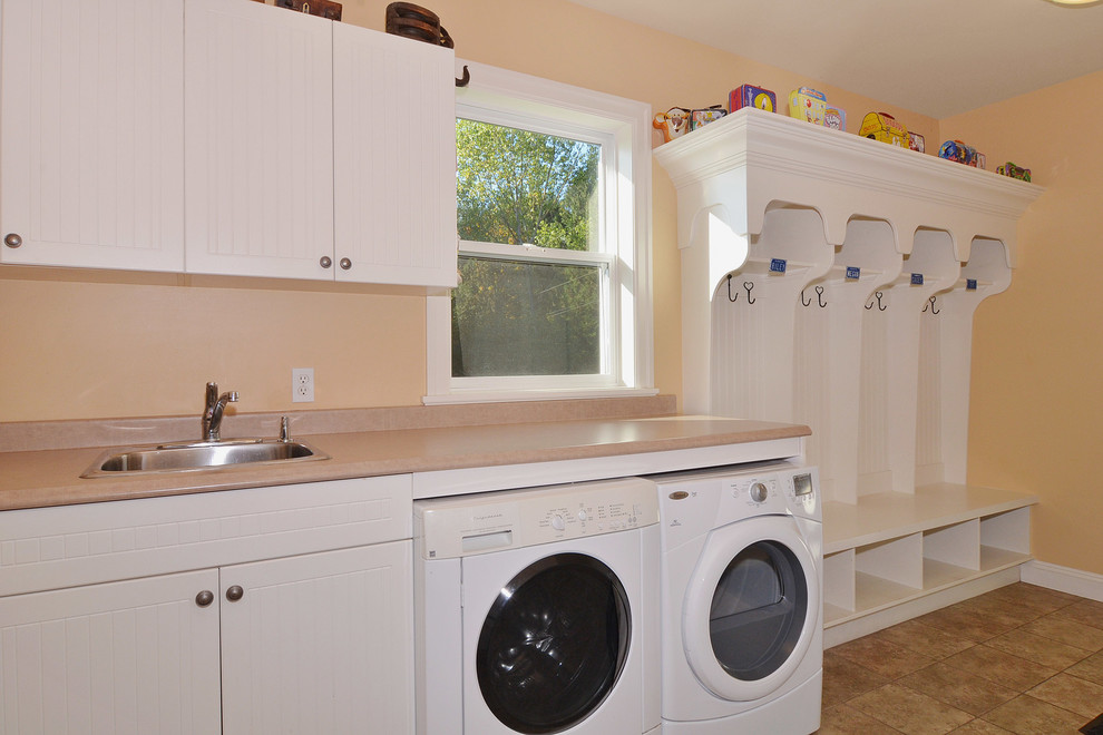 Mid-sized arts and crafts single-wall utility room in Vancouver with white cabinets, laminate benchtops, ceramic floors, a side-by-side washer and dryer, a drop-in sink, flat-panel cabinets and orange walls.