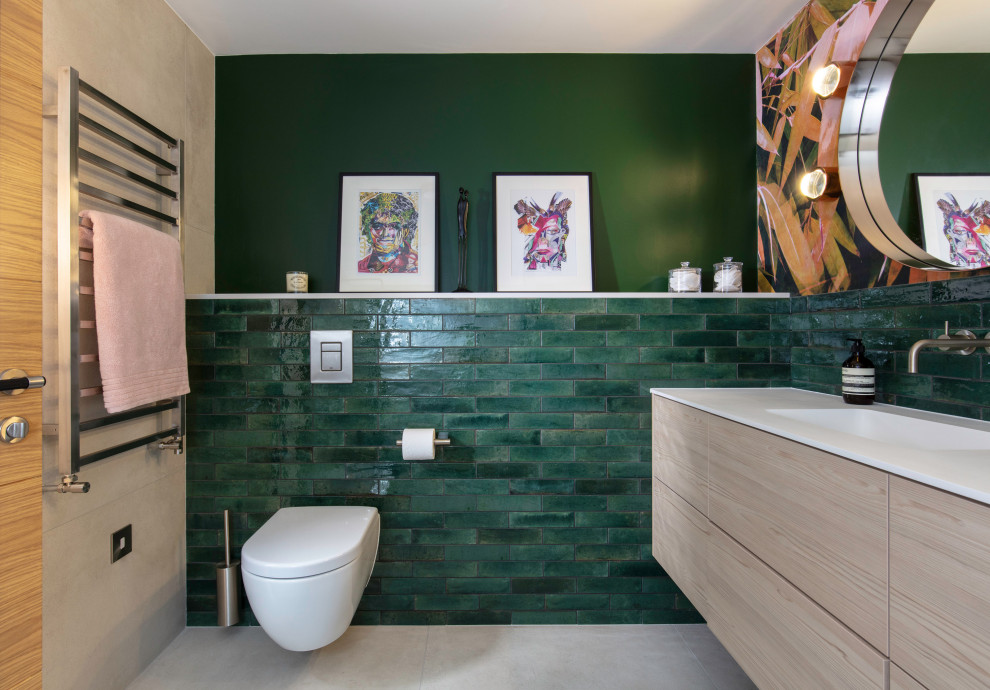 This is an example of a medium sized contemporary cloakroom in London with flat-panel cabinets, light wood cabinets, a wall mounted toilet, green tiles, metro tiles, green walls, porcelain flooring, a built-in sink, beige floors, feature lighting and a floating vanity unit.