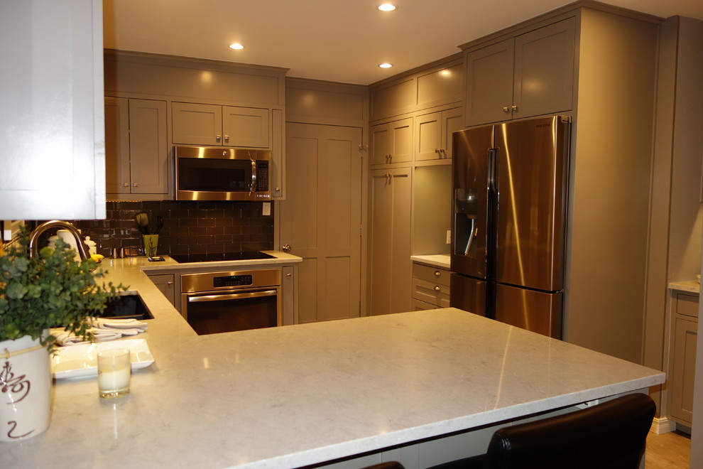Small transitional u-shaped ceramic tile home design photo with an undermount sink, shaker cabinets, gray cabinets, quartz countertops, gray backsplash, glass tile backsplash, stainless steel appliances and a peninsula