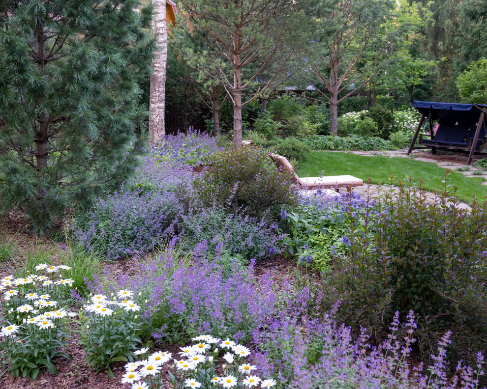 Cette image montre un grand jardin arrière rustique l'été avec un massif de fleurs, une exposition partiellement ombragée, des pavés en pierre naturelle et une clôture en métal.