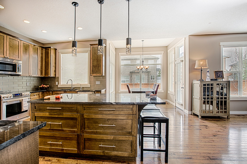 Mid-sized mountain style u-shaped medium tone wood floor and brown floor eat-in kitchen photo in Calgary with an undermount sink, shaker cabinets, medium tone wood cabinets, granite countertops, gray backsplash, glass tile backsplash, stainless steel appliances and an island