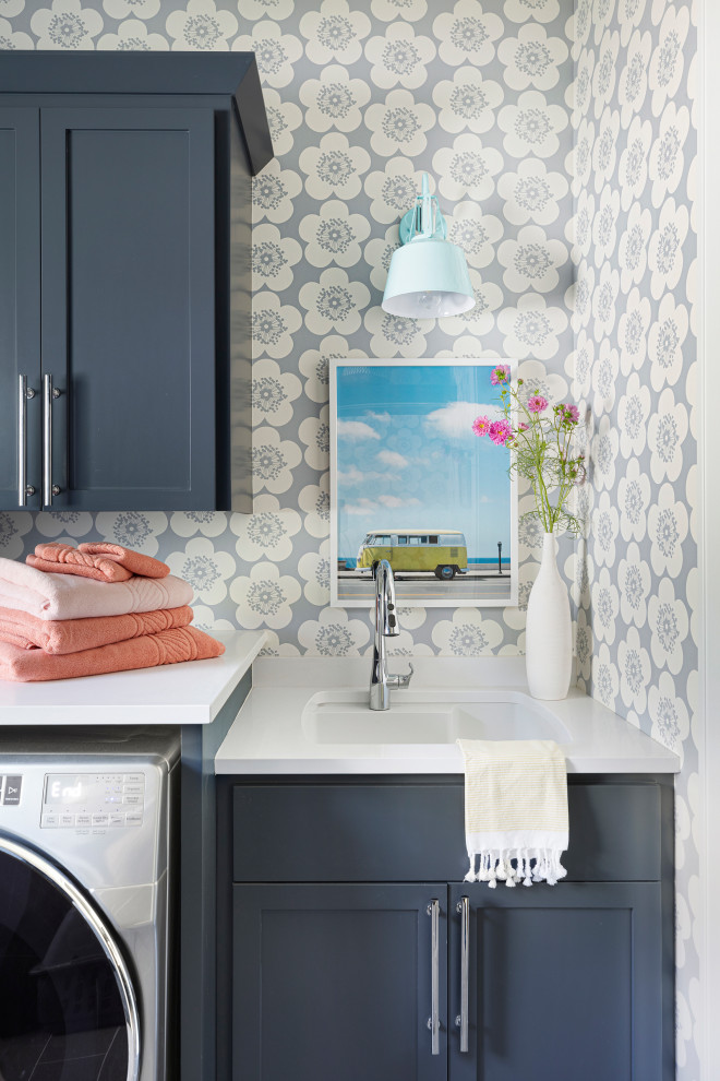 Inspiration for a large beach style l-shaped dedicated laundry room in Minneapolis with an undermount sink, flat-panel cabinets, blue cabinets, quartz benchtops, grey walls, a side-by-side washer and dryer and white benchtop.