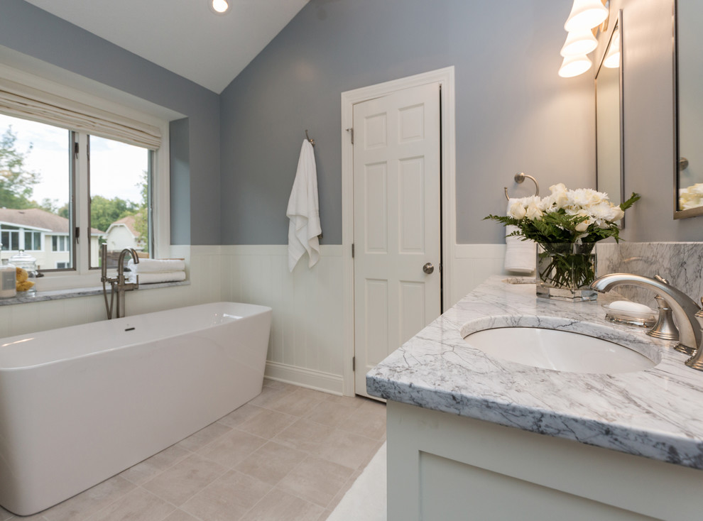 Inspiration for a mid-sized transitional master ceramic tile freestanding bathtub remodel with an undermount sink, furniture-like cabinets, white cabinets, marble countertops, a two-piece toilet and gray walls