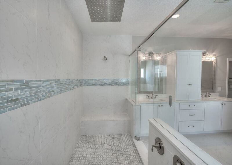 This is an example of a mid-sized beach style master bathroom in Jacksonville with recessed-panel cabinets, white cabinets, a drop-in tub, an alcove shower, blue tile, gray tile, marble, grey walls, marble floors, an undermount sink, grey floor, a hinged shower door and white benchtops.