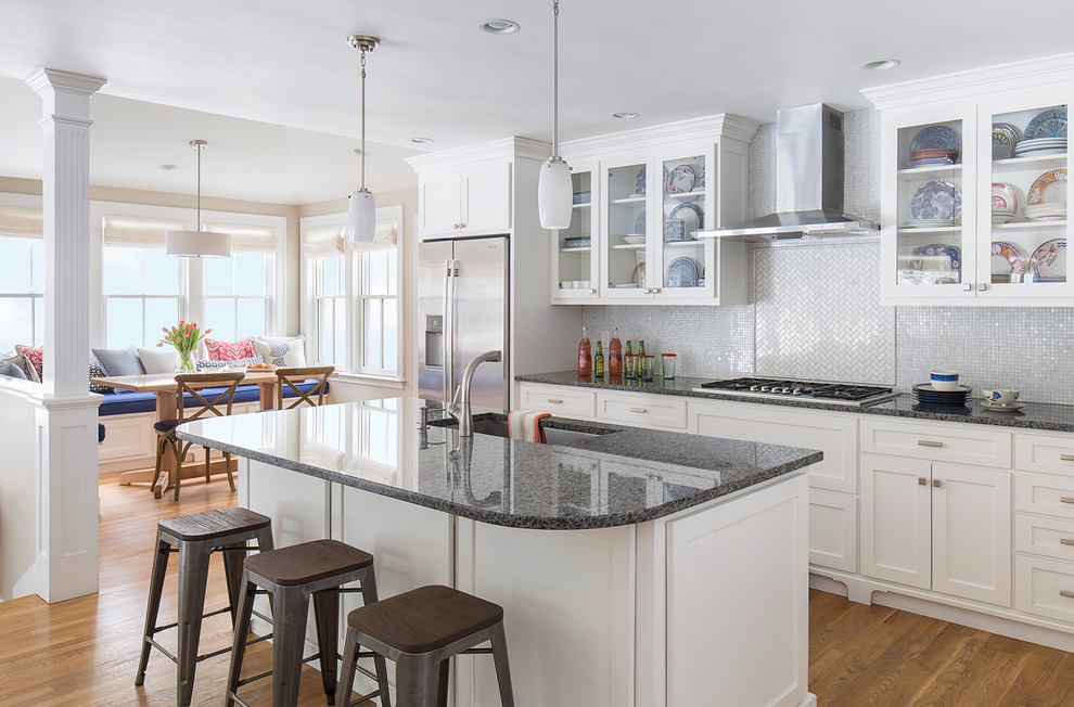 This is an example of a transitional l-shaped open plan kitchen in Boston with a single-bowl sink, glass-front cabinets, white cabinets, granite benchtops, white splashback, stone tile splashback, stainless steel appliances, medium hardwood floors and with island.