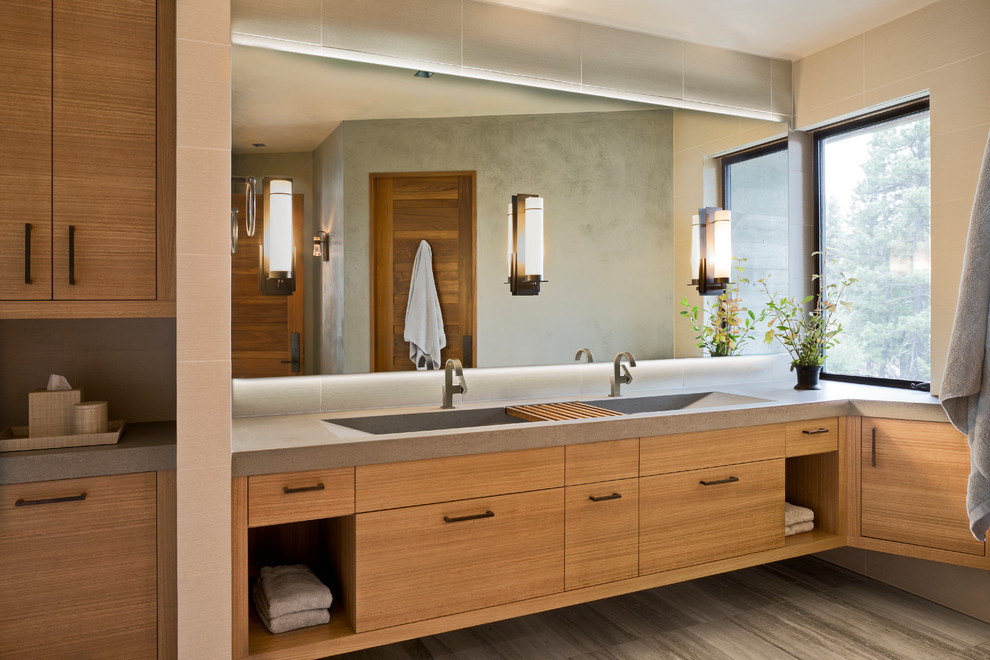 This is an example of a mid-sized country bathroom in Boise with travertine floors, concrete benchtops, flat-panel cabinets, medium wood cabinets, a trough sink and grey floor.