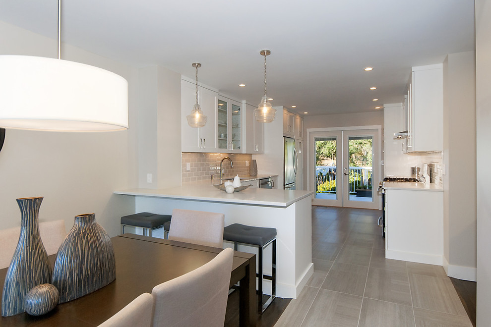 Transitional l-shaped open plan kitchen in Vancouver with a double-bowl sink, shaker cabinets, white cabinets, quartzite benchtops, beige splashback, subway tile splashback, stainless steel appliances, porcelain floors, a peninsula and grey floor.