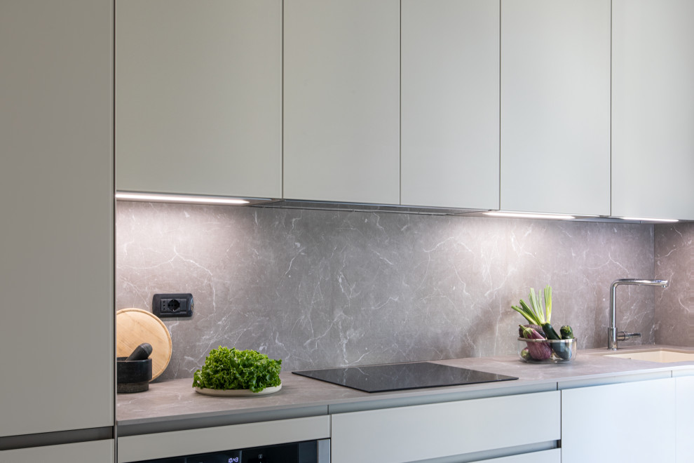 Small contemporary single-wall eat-in kitchen in Milan with an undermount sink, glass-front cabinets, beige cabinets, laminate benchtops, grey splashback, black appliances, porcelain floors, no island, grey floor and grey benchtop.