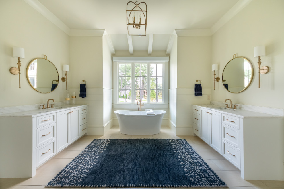 Design ideas for a large transitional master bathroom in Atlanta with recessed-panel cabinets, white cabinets, a freestanding tub, beige walls, ceramic floors, marble benchtops, beige floor, a double vanity, a built-in vanity and white benchtops.
