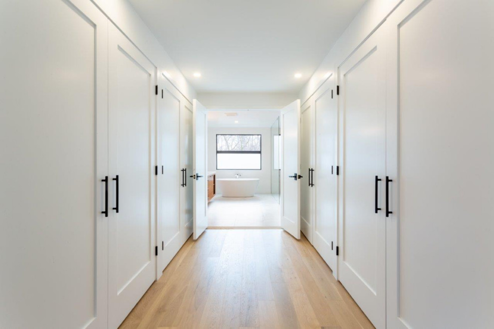 Photo of a large contemporary gender-neutral walk-in wardrobe in Other with shaker cabinets, white cabinets and light hardwood floors.