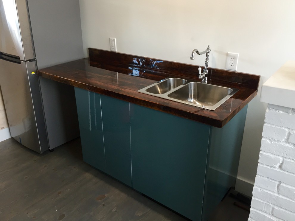 This is an example of a small country single-wall kitchen in Portland Maine with a double-bowl sink, wood benchtops, grey floor, flat-panel cabinets, green cabinets, stainless steel appliances and dark hardwood floors.