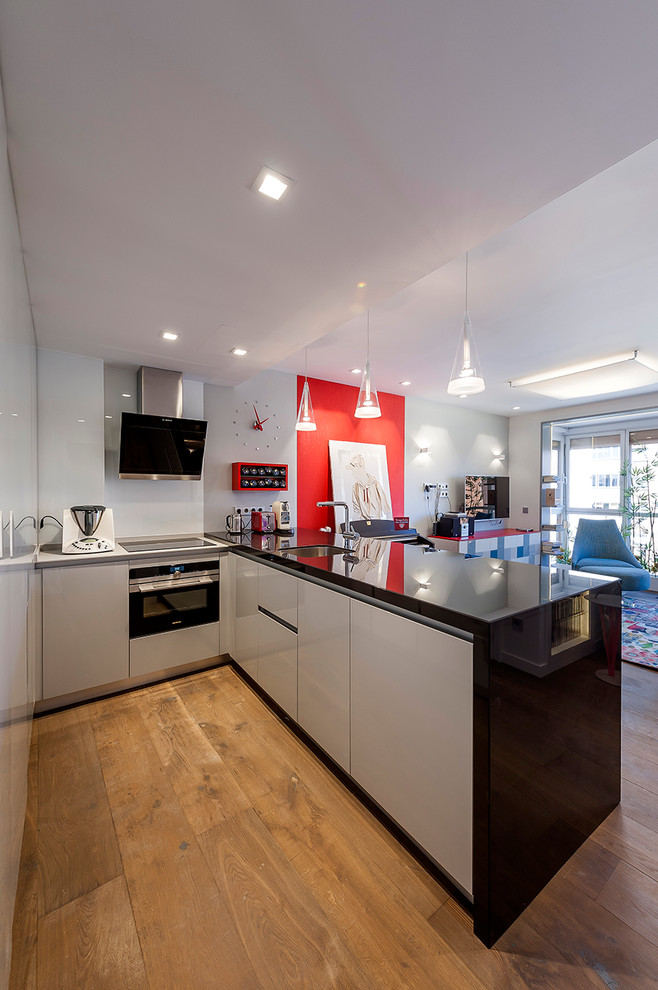 Small contemporary l-shaped eat-in kitchen in Madrid with a single-bowl sink, flat-panel cabinets, white cabinets, glass benchtops, black splashback, panelled appliances, dark hardwood floors and with island.