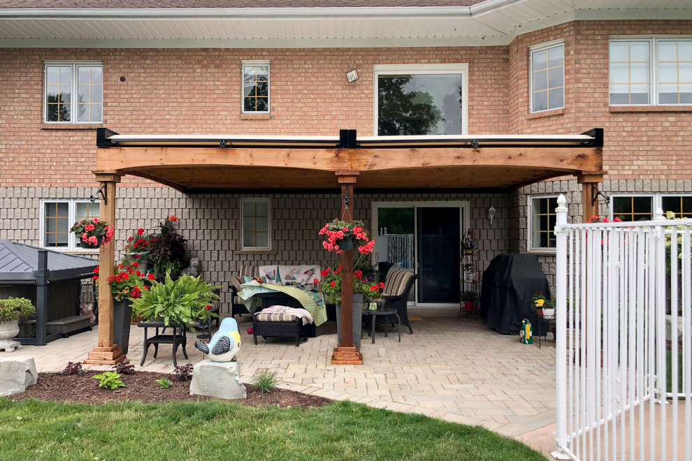 Design ideas for a mid-sized traditional backyard patio in Toronto with natural stone pavers and a pergola.