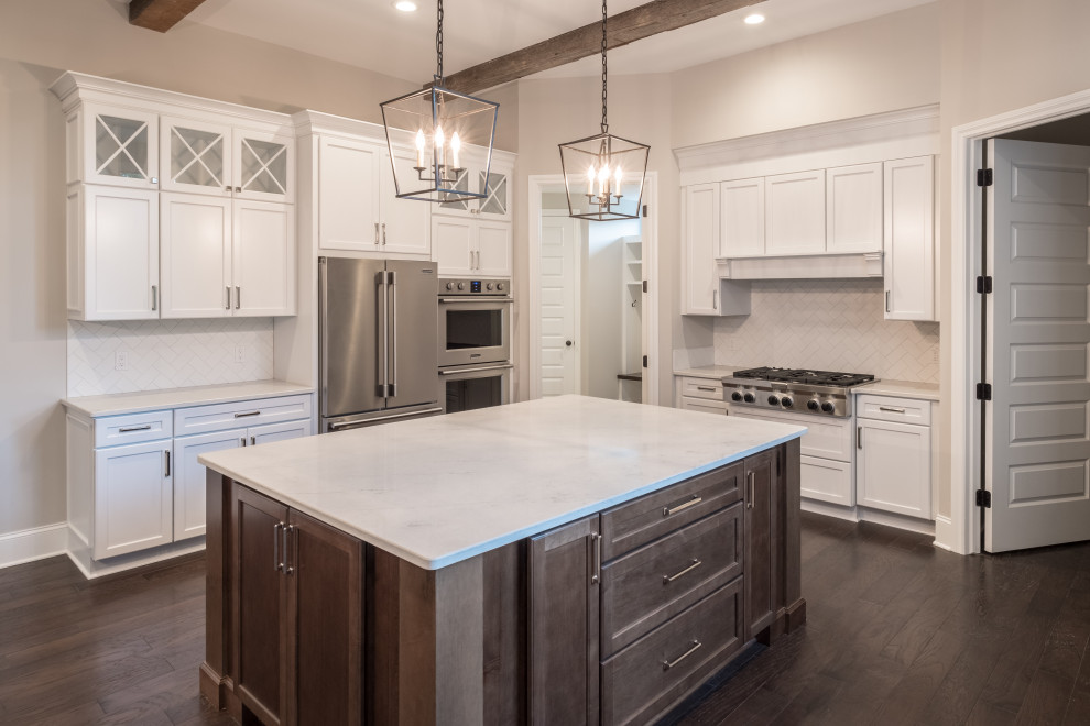 Photo of a large country u-shaped eat-in kitchen in Detroit with a farmhouse sink, white cabinets, white splashback, stainless steel appliances, dark hardwood floors, with island, brown floor, white benchtop and exposed beam.