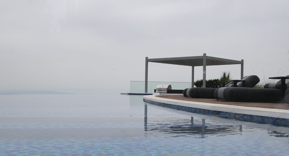 Идея дизайна: огромный бассейн-инфинити произвольной формы на заднем дворе в стиле модернизм с настилом