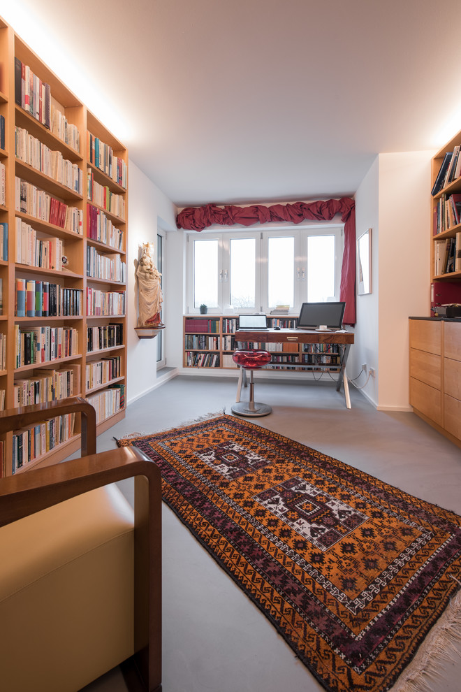 Lesezimmer ohne Kamin mit weißer Wandfarbe, Betonboden, freistehendem Schreibtisch und grauem Boden in Cologne