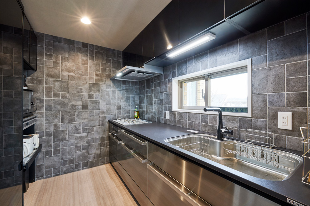 Photo of a small industrial galley kitchen in Other with an undermount sink, flat-panel cabinets, stainless steel cabinets, grey splashback, porcelain splashback, stainless steel appliances, no island, beige floor and black benchtop.