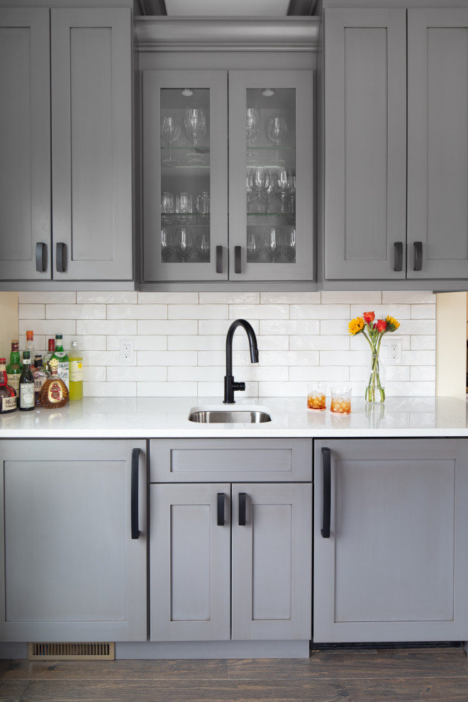 Transitional medium tone wood floor and brown floor kitchen photo with an undermount sink, shaker cabinets, gray cabinets, quartzite countertops, white backsplash, subway tile backsplash and white countertops