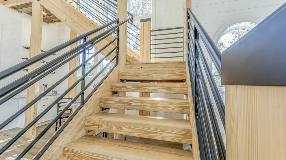 This is an example of a large beach style wood u-shaped staircase in Miami with open risers and metal railing.