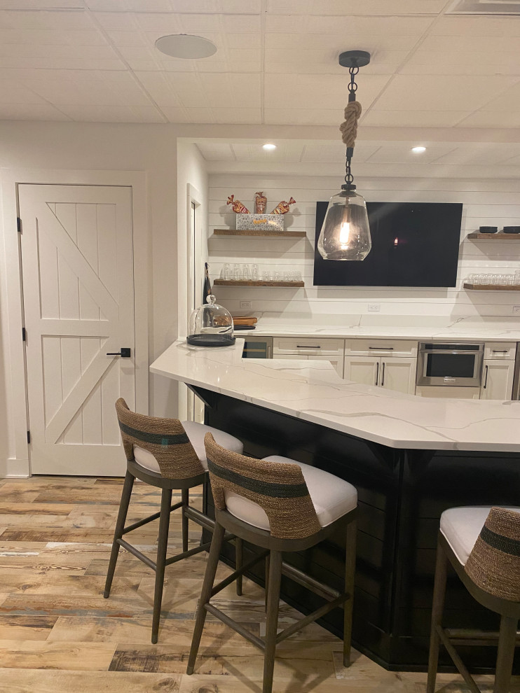 Inspiration for a mid-sized transitional u-shaped wet bar in Newark with an undermount sink, recessed-panel cabinets, white cabinets, quartz benchtops, white splashback, shiplap splashback, light hardwood floors, brown floor and white benchtop.