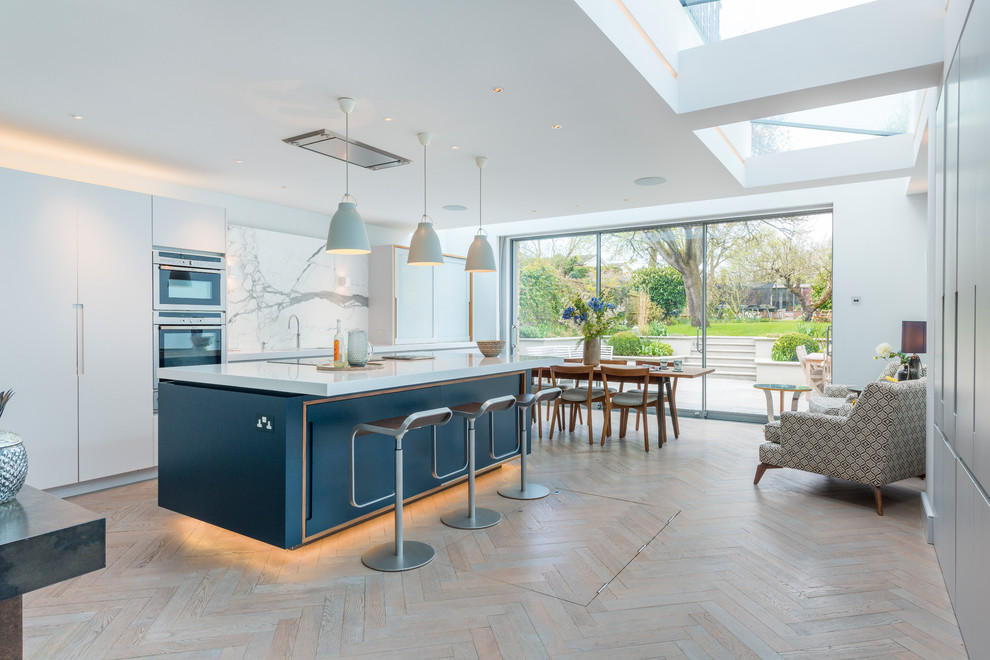 Inspiration for a large contemporary single-wall eat-in kitchen in Other with an undermount sink, flat-panel cabinets, white cabinets, white splashback, marble splashback, light hardwood floors, with island and beige floor.