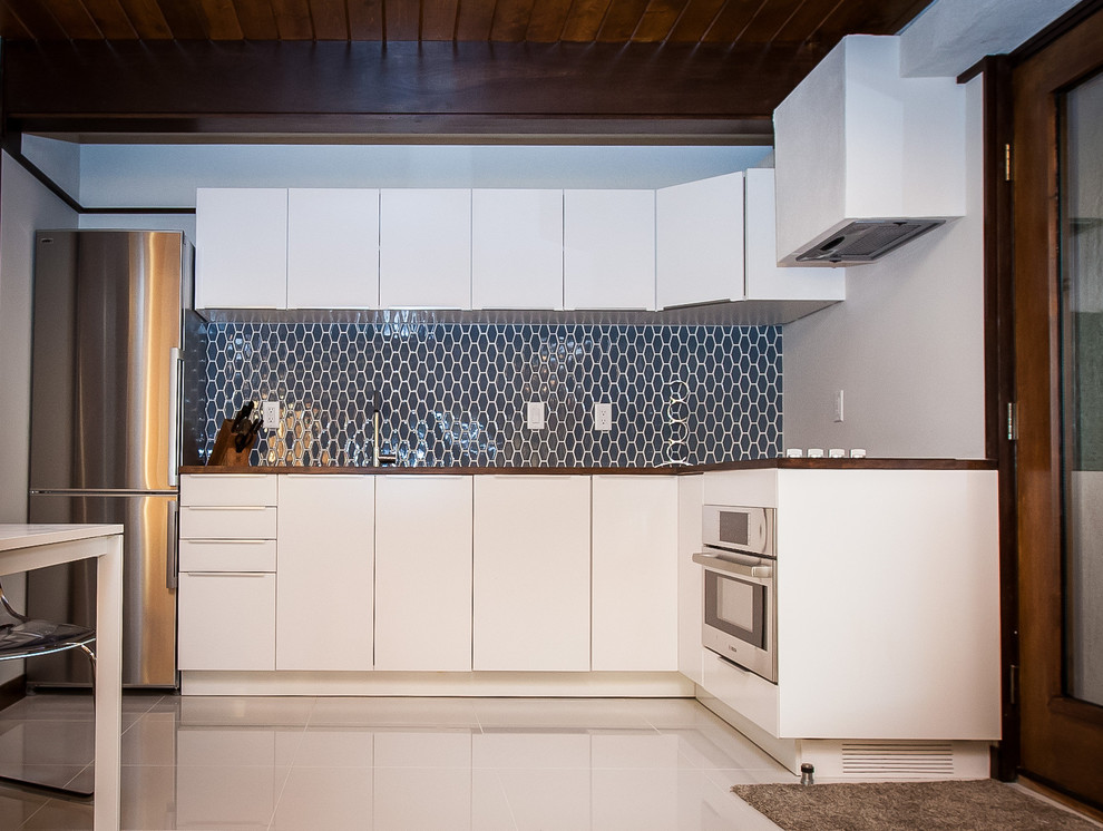 Small midcentury l-shaped open plan kitchen in Salt Lake City with flat-panel cabinets, white cabinets, wood benchtops, blue splashback, glass tile splashback, stainless steel appliances and terrazzo floors.