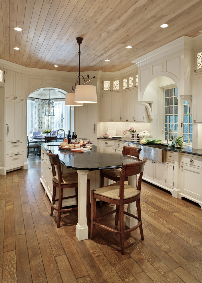 Design ideas for a mid-sized traditional u-shaped eat-in kitchen in New York with a farmhouse sink, shaker cabinets, white cabinets, white splashback, medium hardwood floors, with island, marble benchtops, ceramic splashback and stainless steel appliances.