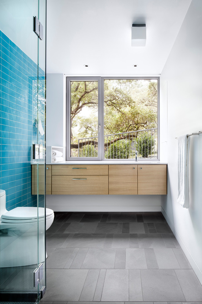 Mid-sized midcentury 3/4 bathroom in Austin with flat-panel cabinets, light wood cabinets, a one-piece toilet, ceramic tile, white walls, porcelain floors, solid surface benchtops, grey floor, white benchtops and blue tile.