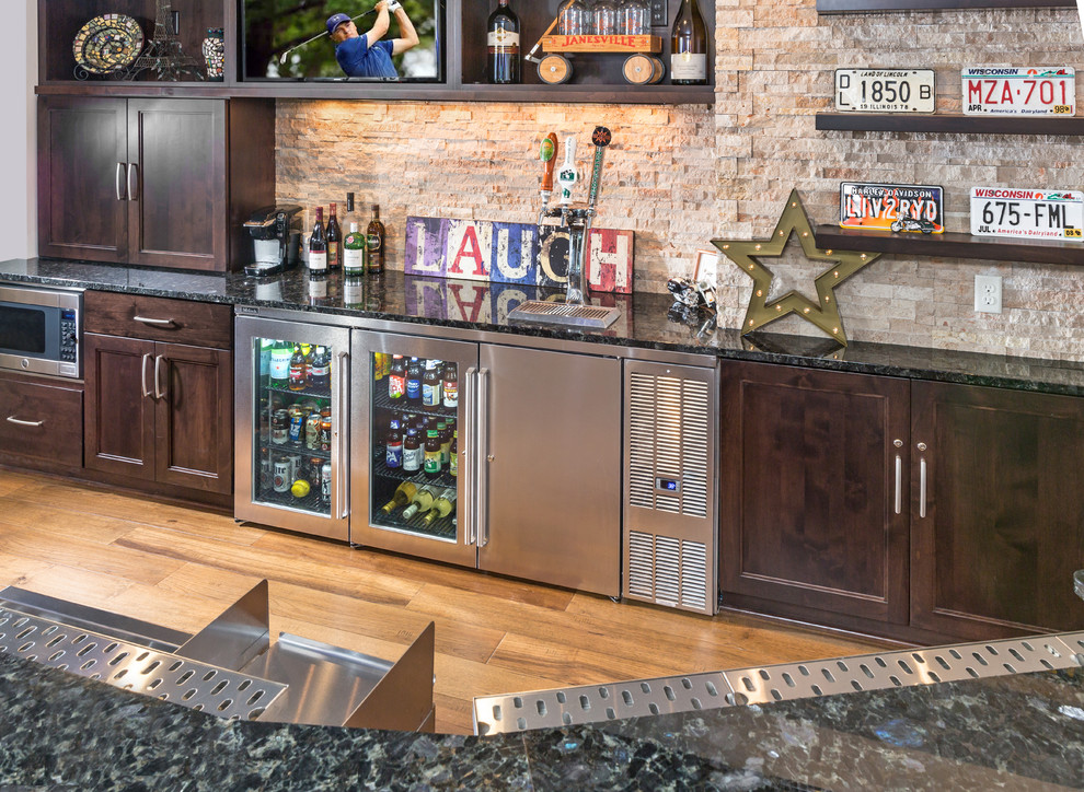 Photo of a large transitional u-shaped wet bar in Milwaukee with recessed-panel cabinets, dark wood cabinets, granite benchtops, beige splashback, stone tile splashback and medium hardwood floors.