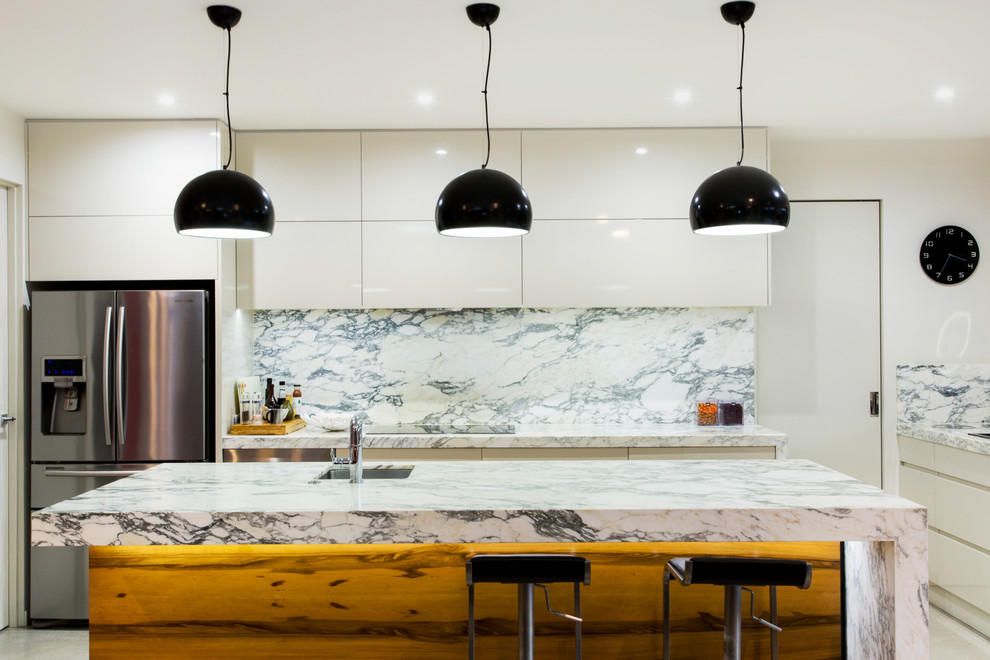 Mid-sized contemporary l-shaped eat-in kitchen in Geelong with a drop-in sink, marble benchtops, porcelain splashback, with island, stainless steel appliances, flat-panel cabinets, white cabinets, concrete floors, multi-coloured splashback and orange benchtop.