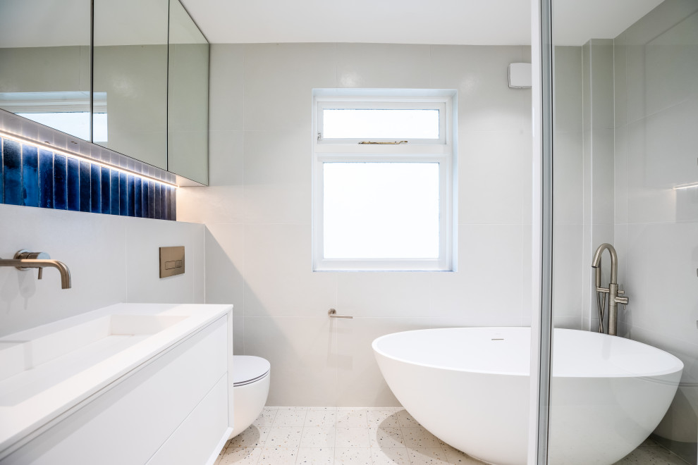 Inspiration for a small modern kids bathroom in London with glass-front cabinets, a freestanding tub, a corner shower, a wall-mount toilet, white tile, porcelain tile, porcelain floors, an integrated sink, soapstone benchtops, a sliding shower screen, white benchtops, a single vanity and a floating vanity.