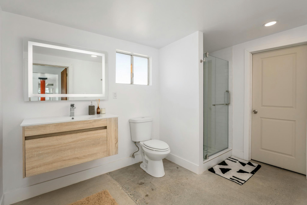 Идея дизайна: маленькая ванная комната в стиле модернизм с плоскими фасадами, светлыми деревянными фасадами, душем в нише, раздельным унитазом, белой плиткой, белыми стенами, бетонным полом, душевой кабиной, монолитной раковиной, столешницей из искусственного камня, бежевым полом, душем с распашными дверями, белой столешницей, тумбой под одну раковину и подвесной тумбой для на участке и в саду