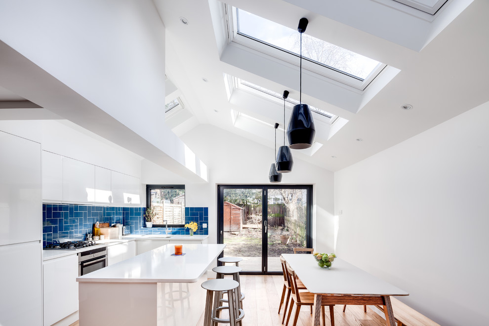 Inspiration for a mid-sized contemporary eat-in kitchen in London with an undermount sink, flat-panel cabinets, white cabinets, blue splashback, stainless steel appliances, light hardwood floors and with island.