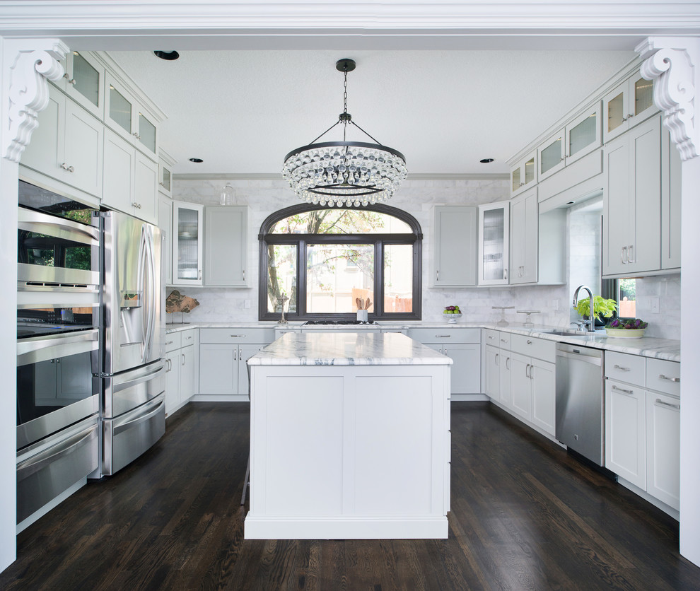 Design ideas for a traditional u-shaped kitchen in Kansas City with an undermount sink, shaker cabinets, white cabinets, white splashback, stainless steel appliances, dark hardwood floors, with island and marble benchtops.