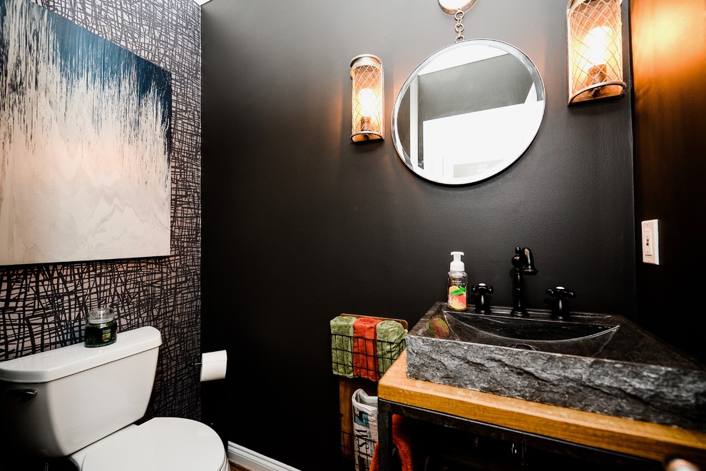 Design ideas for a small industrial powder room in Other with furniture-like cabinets, medium wood cabinets, a two-piece toilet, black walls, medium hardwood floors, a vessel sink, wood benchtops and brown floor.