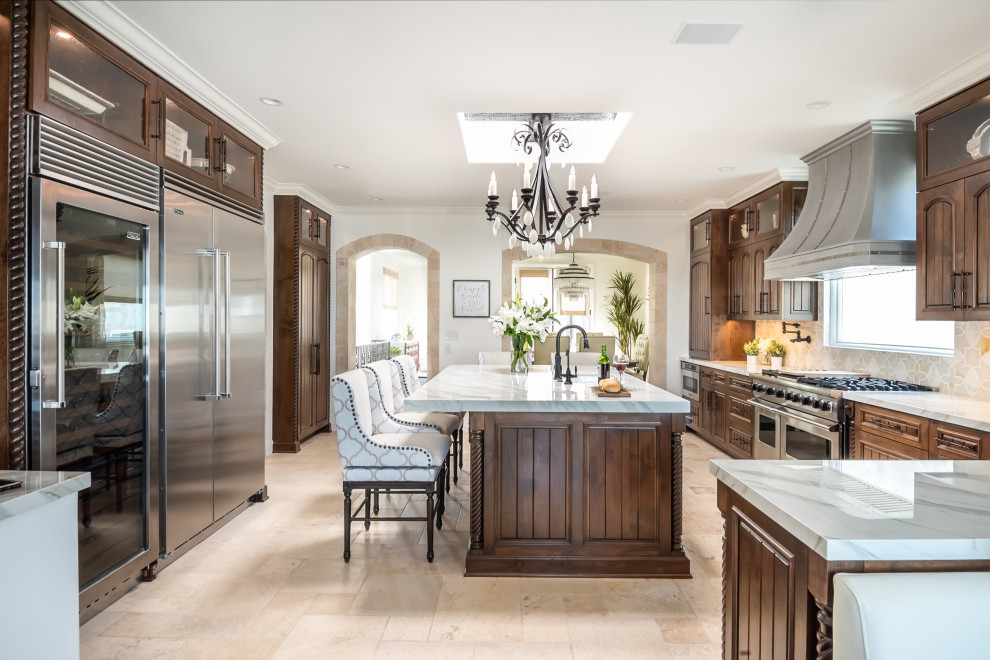 Photo of a large kitchen in Los Angeles with an undermount sink, dark wood cabinets, stainless steel appliances, limestone floors, with island and beige floor.