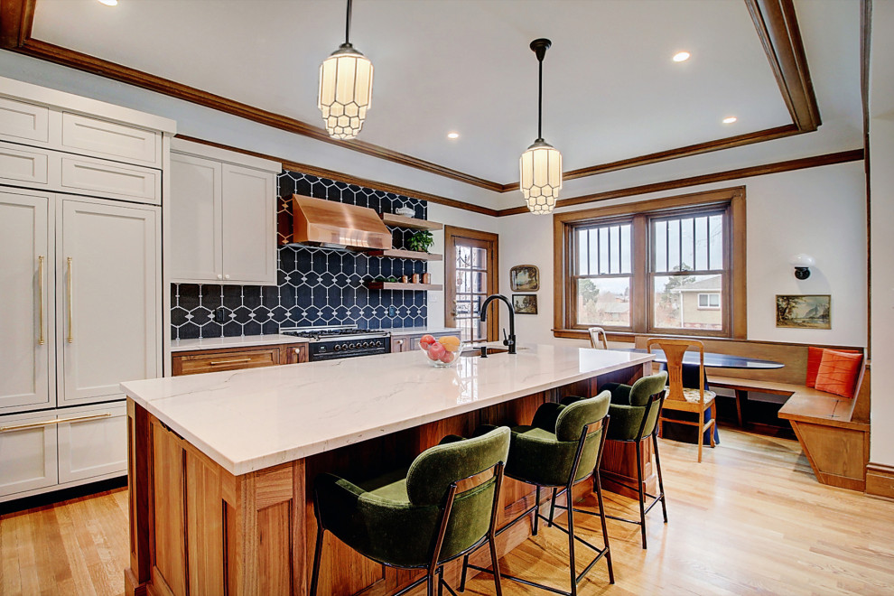 Example of a large arts and crafts light wood floor, brown floor and coffered ceiling kitchen design in Denver with an undermount sink, recessed-panel cabinets, medium tone wood cabinets, marble countertops, black backsplash, mosaic tile backsplash, paneled appliances, an island and white countertops