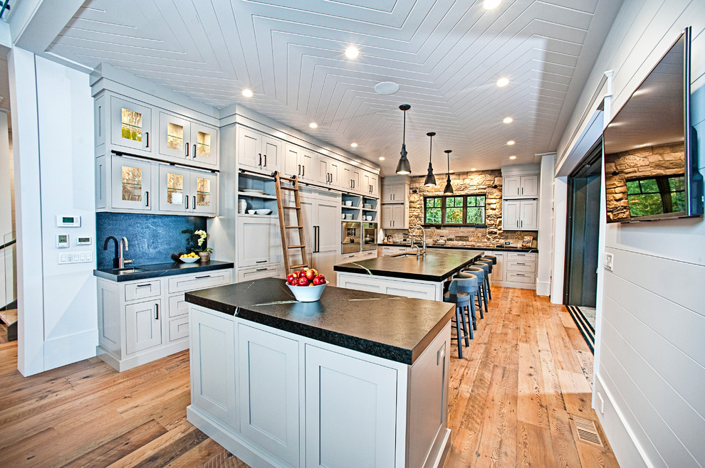 Eat-in kitchen - large rustic l-shaped medium tone wood floor and brown floor eat-in kitchen idea with an undermount sink, shaker cabinets, gray cabinets, soapstone countertops, black backsplash, stone slab backsplash, stainless steel appliances and two islands