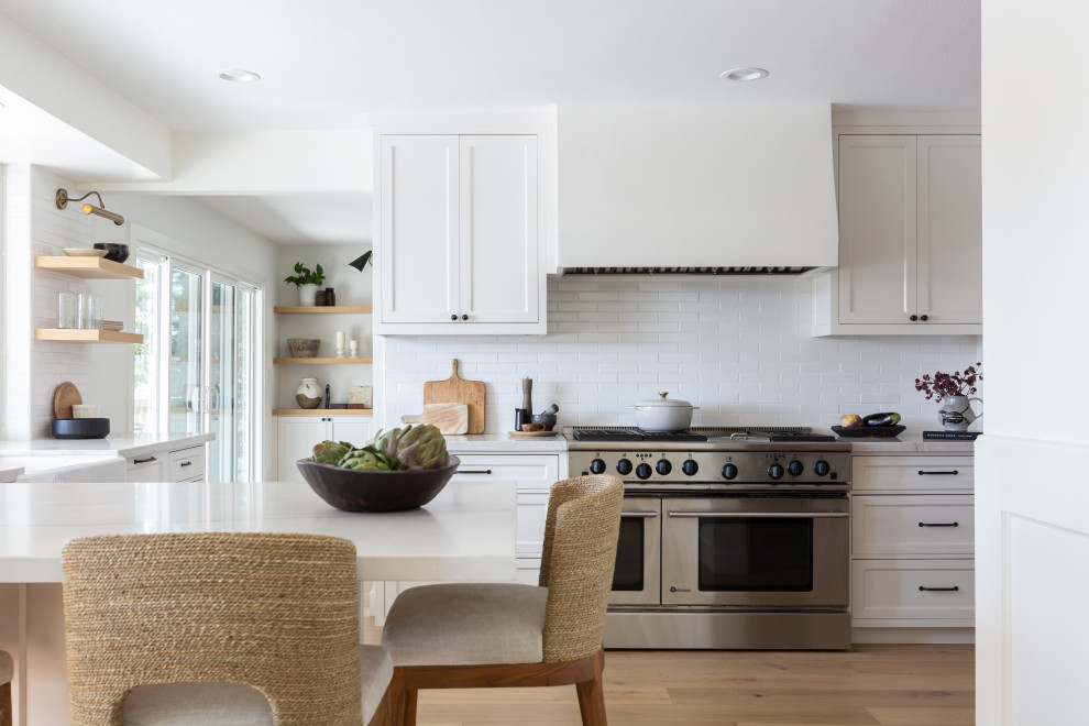 Transitional u-shaped eat-in kitchen in San Diego with a farmhouse sink, beaded inset cabinets, white cabinets, quartzite benchtops, ceramic splashback, stainless steel appliances, light hardwood floors, white benchtop and white splashback.