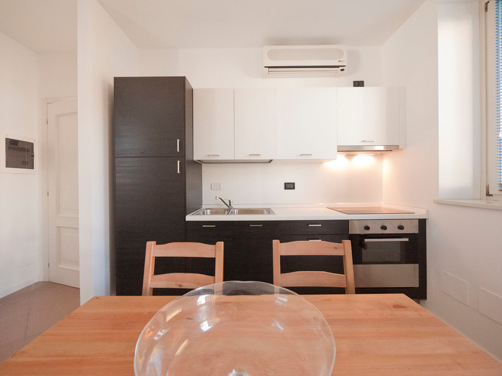 Photo of a small modern single-wall eat-in kitchen in Milan with a double-bowl sink, flat-panel cabinets, dark wood cabinets, laminate benchtops, white splashback, stainless steel appliances, ceramic floors and no island.