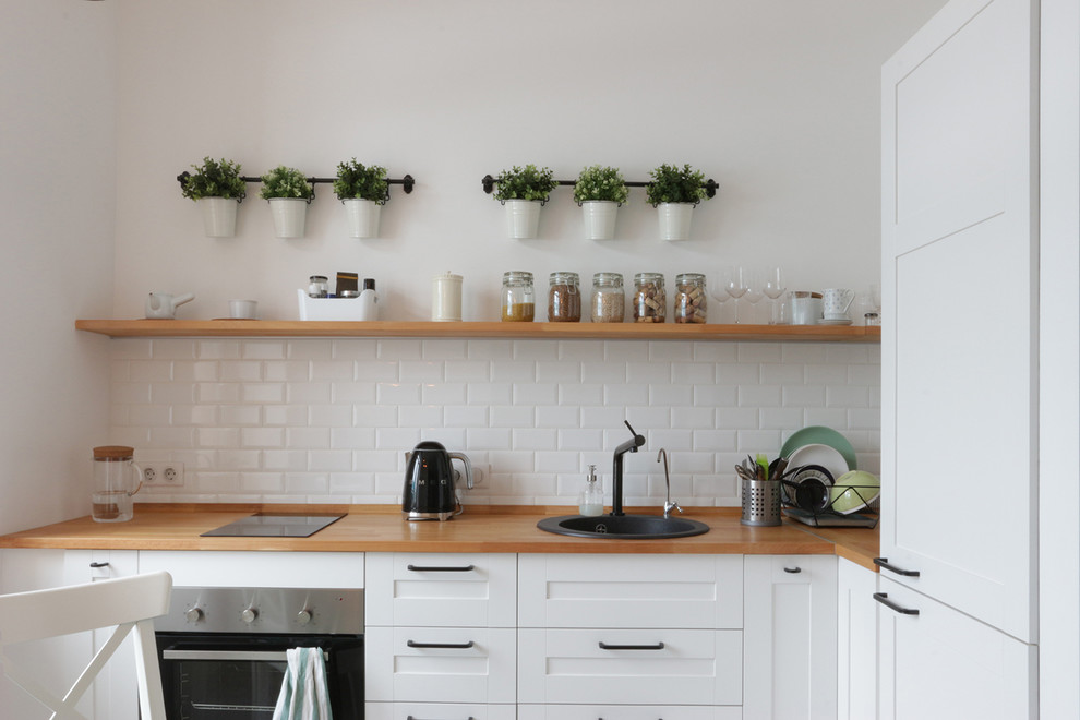 Transitional l-shaped separate kitchen in Moscow with a drop-in sink, shaker cabinets, white cabinets, wood benchtops, white splashback, subway tile splashback, no island, brown benchtop and stainless steel appliances.