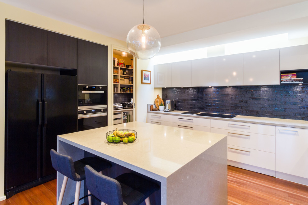 This is an example of a large contemporary u-shaped open plan kitchen in Melbourne with flat-panel cabinets, quartz benchtops, black splashback, subway tile splashback, medium hardwood floors, with island and grey benchtop.