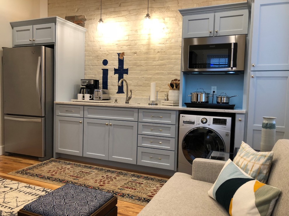 Open concept kitchen - small transitional single-wall light wood floor and brown floor open concept kitchen idea with recessed-panel cabinets, gray cabinets, no island, an undermount sink, marble countertops, white backsplash, brick backsplash, stainless steel appliances and gray countertops