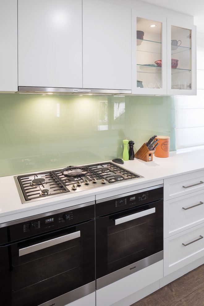 Modern kitchen in Perth with flat-panel cabinets, white cabinets, quartz benchtops, green splashback, glass sheet splashback, stainless steel appliances and white benchtop.