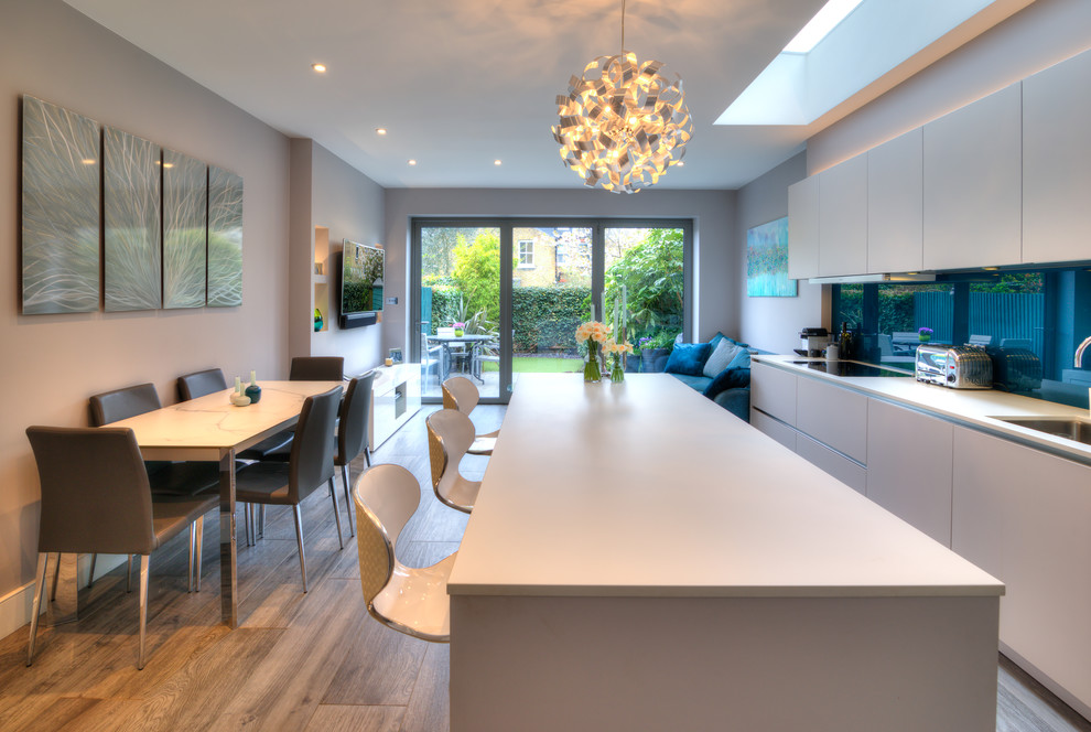 Photo of a mid-sized contemporary single-wall open plan kitchen in Other with flat-panel cabinets, white cabinets, with island, white benchtop, an undermount sink and glass sheet splashback.