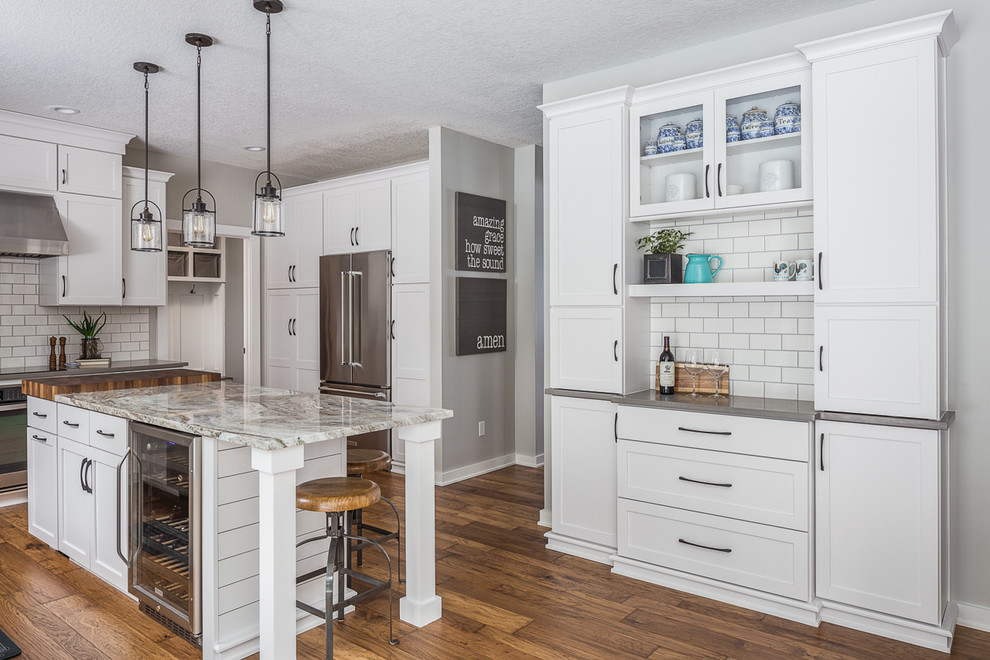 Example of a large transitional l-shaped eat-in kitchen design with a drop-in sink, recessed-panel cabinets, white cabinets, quartzite countertops, white backsplash, stainless steel appliances and an island